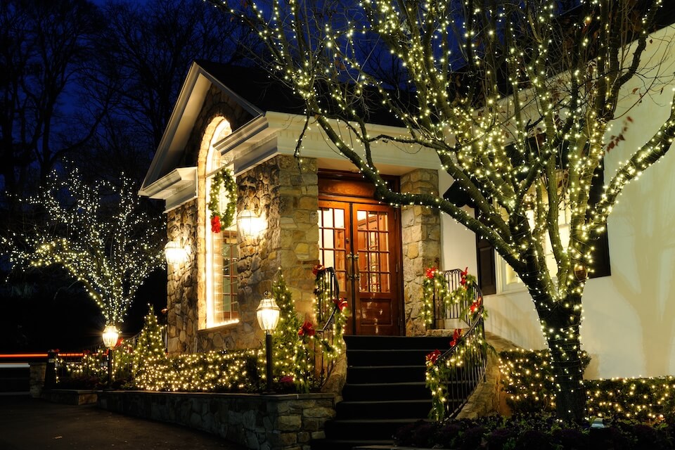 Vue d'une maison avec ses arbres, arbustes et rampes d'escalier illuminés pour le temps des Fêtes
